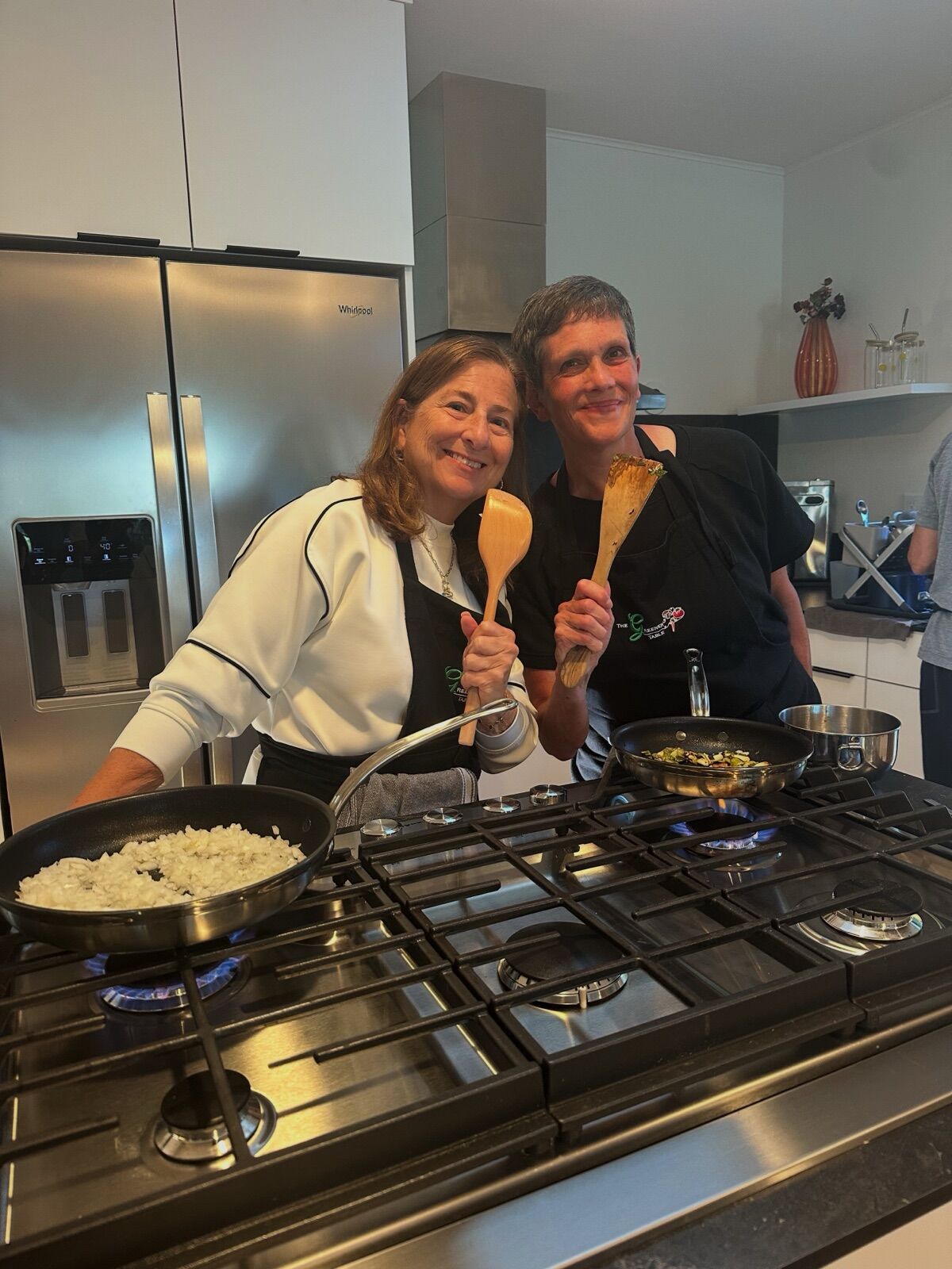 Two guests cooking side by side at the stove with wooden spoons