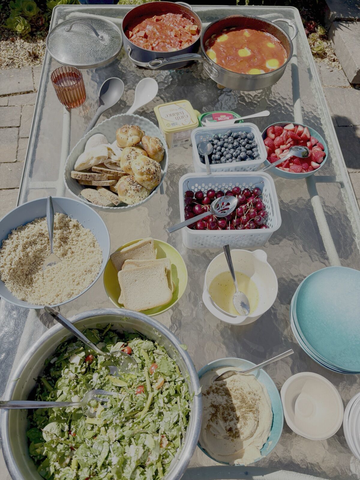 An overhead view of shakshuka, salads, fruit and sides on an outdoor table