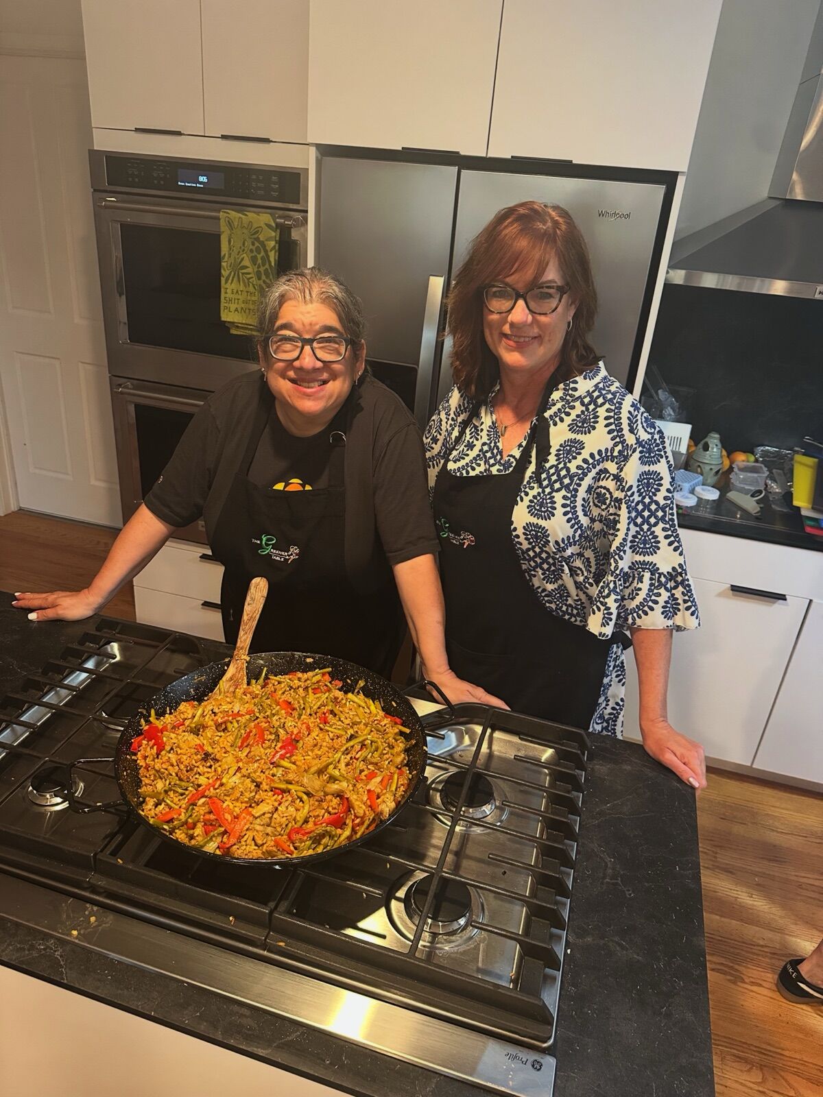 Two cooks smiling over a pan of paella on the stove
