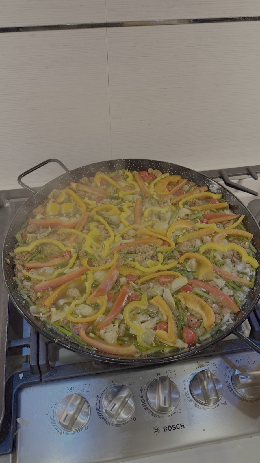 A paella pan topped with red, yellow and green peppers on the stove