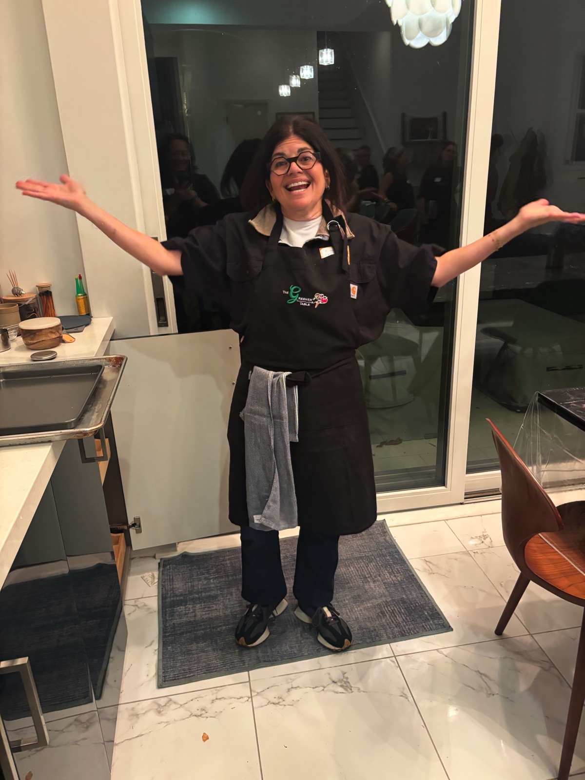 A host in a Greener Table apron welcoming guests with open arms