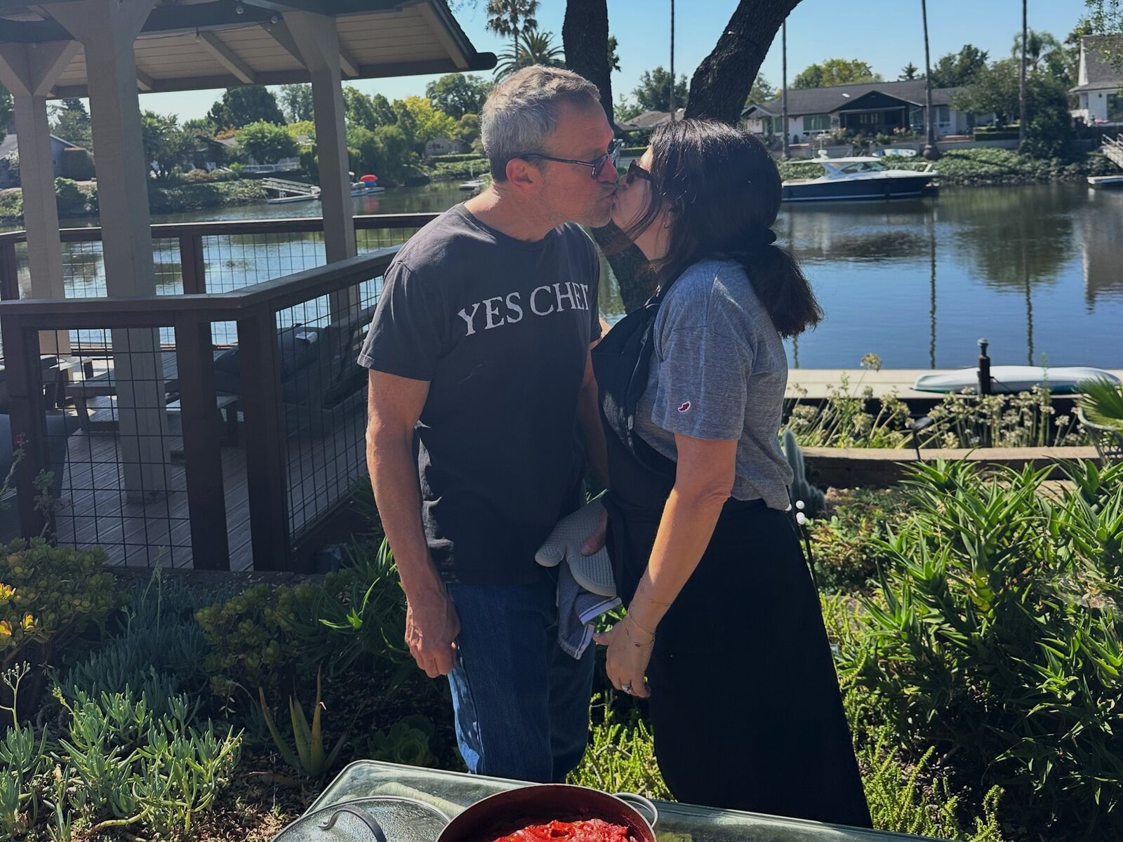 Stacy and Noah sharing a kiss by the water, with pans of shakshuka in front of them