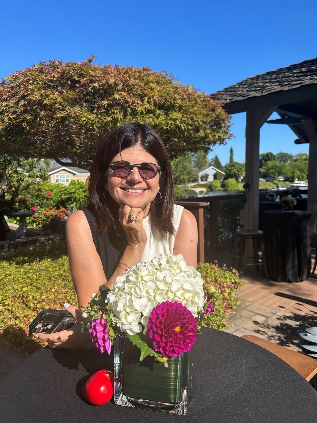 Stacy smiling at an outdoor table with a vase of hydrangeas and dahlias